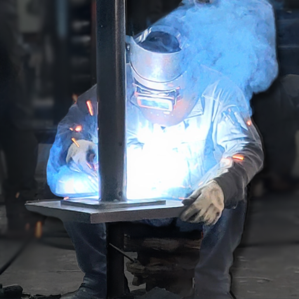 工場で鋼製ポールのベースプレートを溶接している金属加工の作業風景